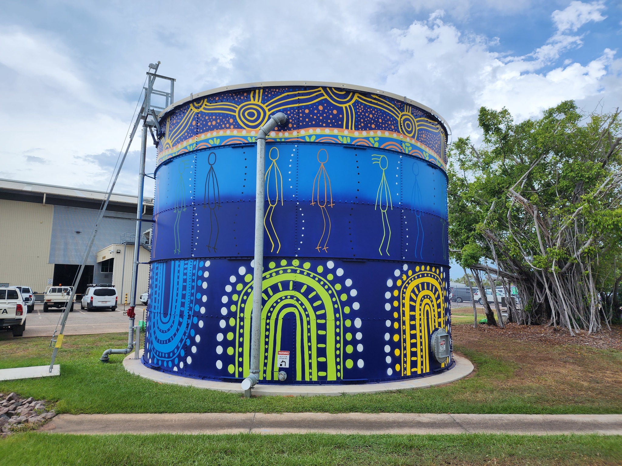 Reconciliation artwork design painted on a fire suppression tank at a Power and Water office site in Darwin (Ben Hammond Complex). The top band of the artwork depicts the four elements of fire, earth, air and water and how the elements are connected or work together, reflecting a journey.  The middle band depicts the reconciliation of Aboriginal peoples and the wider community, and building relationships through mutual respect, equity and equality. The bottom band represents two-way learning and particularly the learning journey between grandparents, parents and children. 